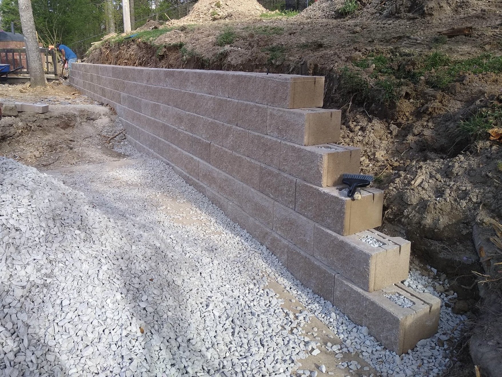 Construction of a stone retaining wall with concrete blocks, with gravel and construction tools nearby.
