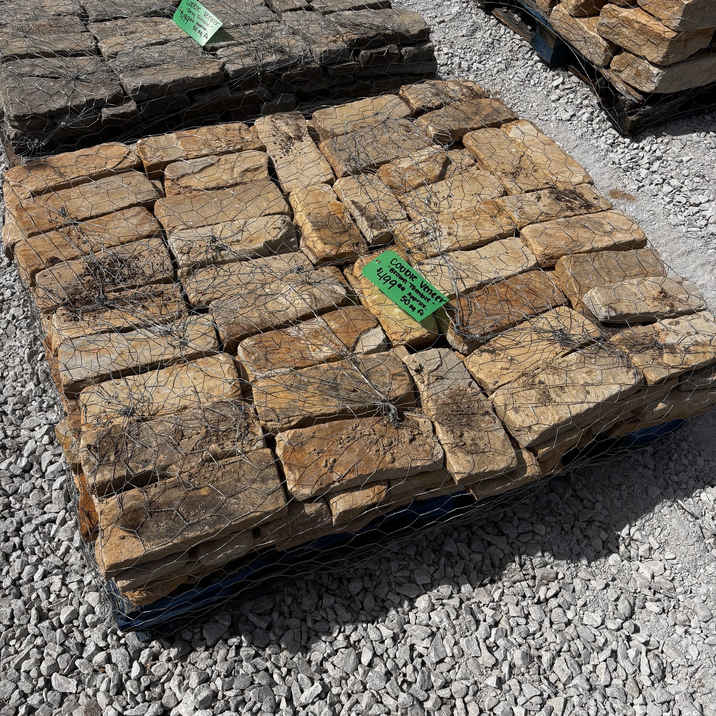 Stacks of brown and gray natural stones stored in plastic pallets and secured with wire mesh, with green price tags attached.