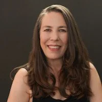 A woman with long brown hair smiling in front of a neutral background.