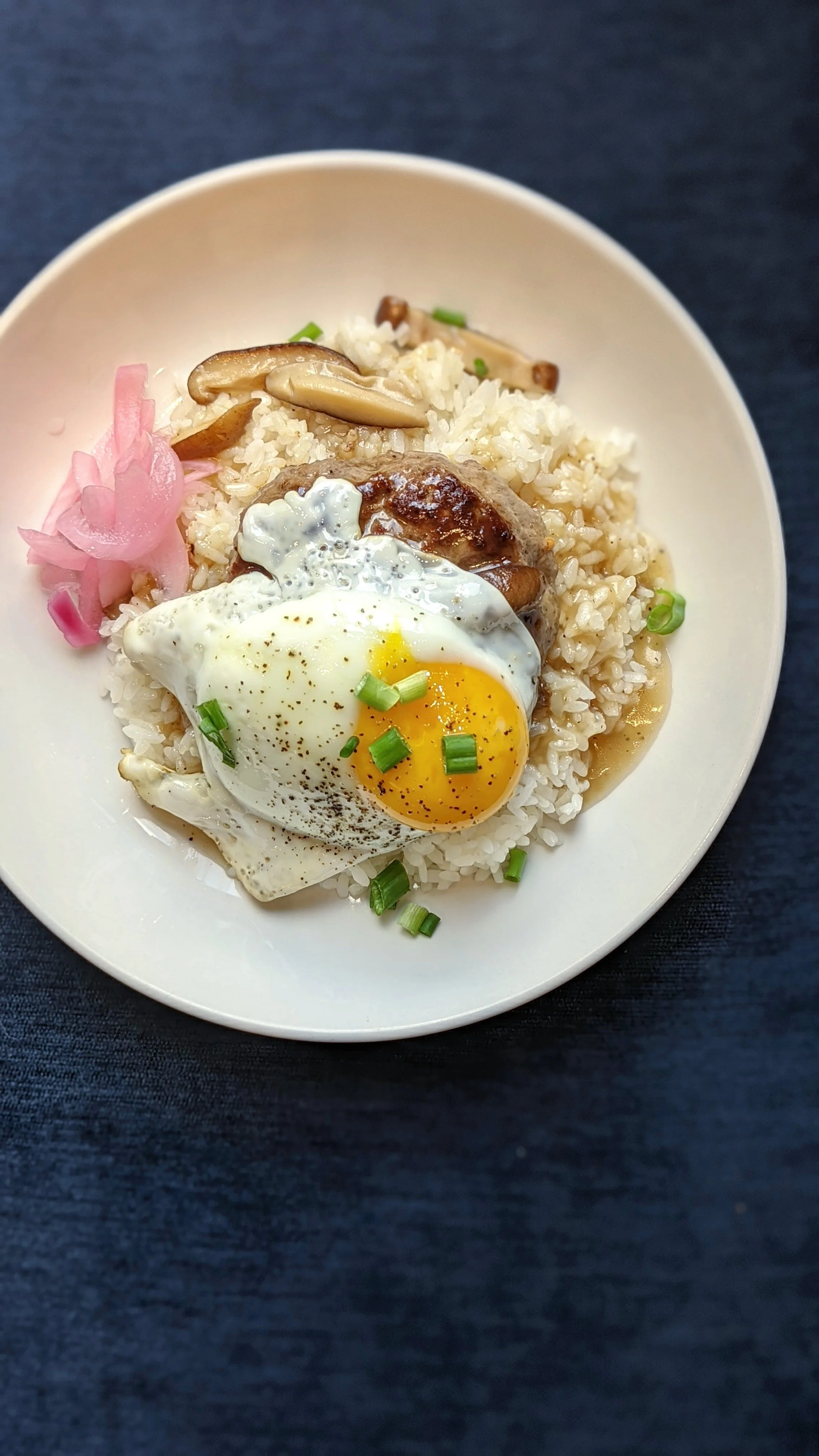 A bowl of rice topped with fried egg, grilled chicken, mushrooms, green onions, and pickled ginger.