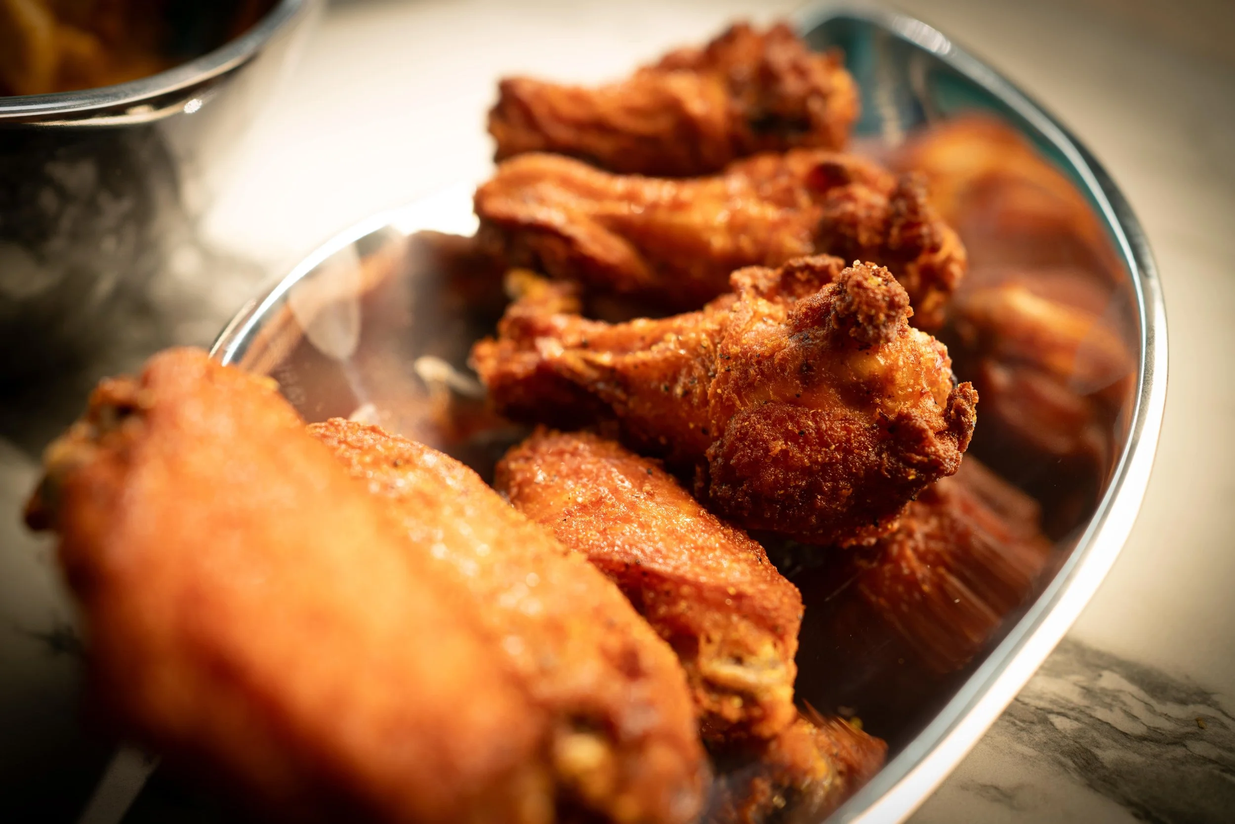 Fried chicken drumsticks with a crispy, seasoned coating in a metal serving dish.