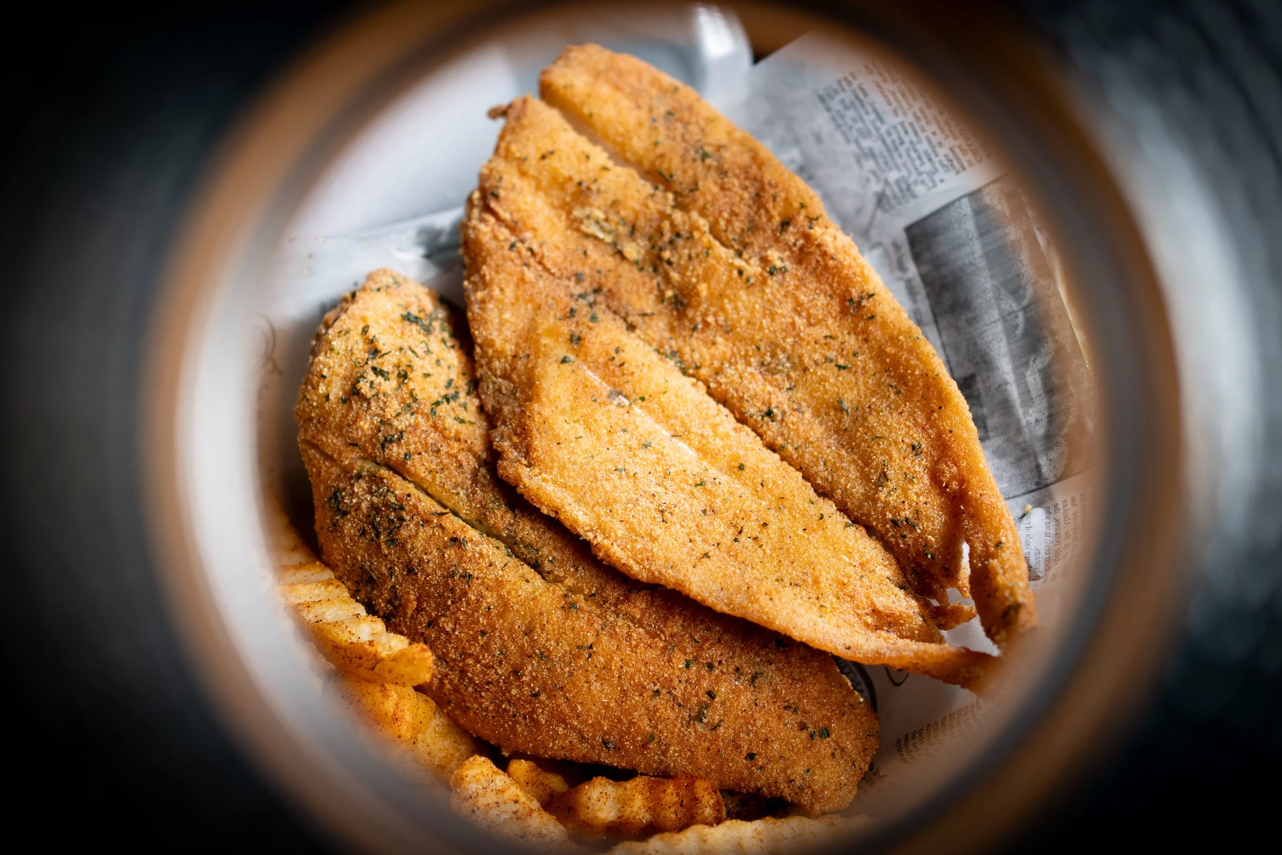 Breaded and fried fish fillets with specks of herbs, inside a jar with the opening framing the view
