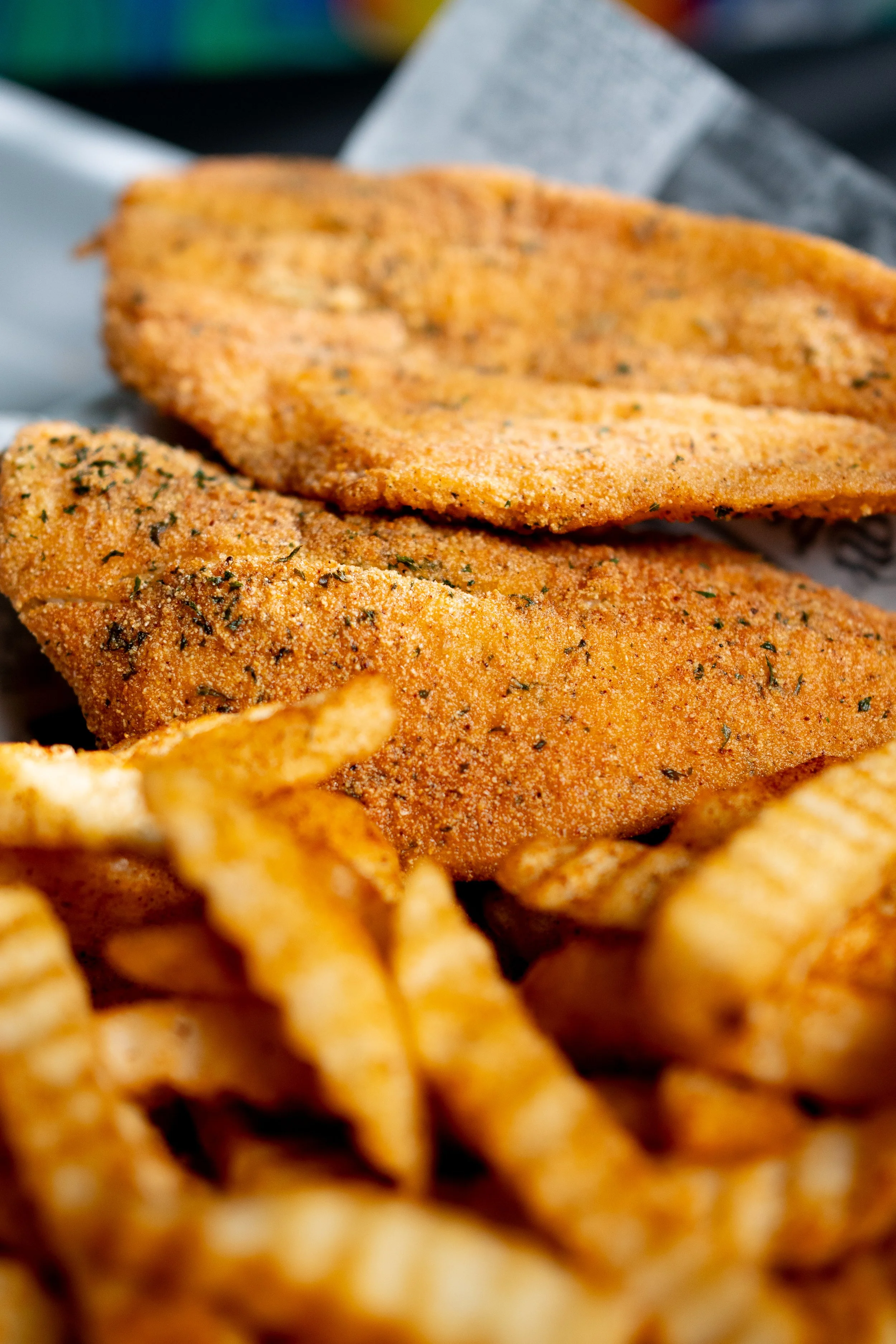 Close-up of fried fish fillets with crispy, seasoned coating and French fries in the foreground.