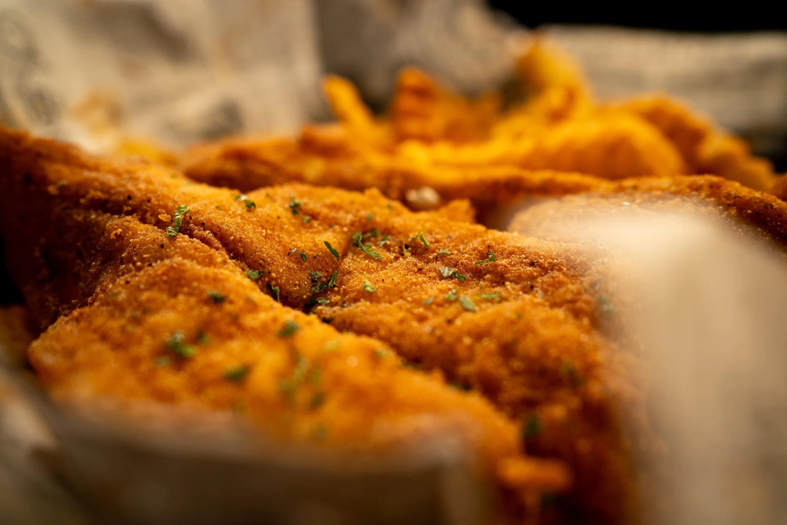 Close-up of seasoned and fried fish fillets with parsley, with French fries in the background.