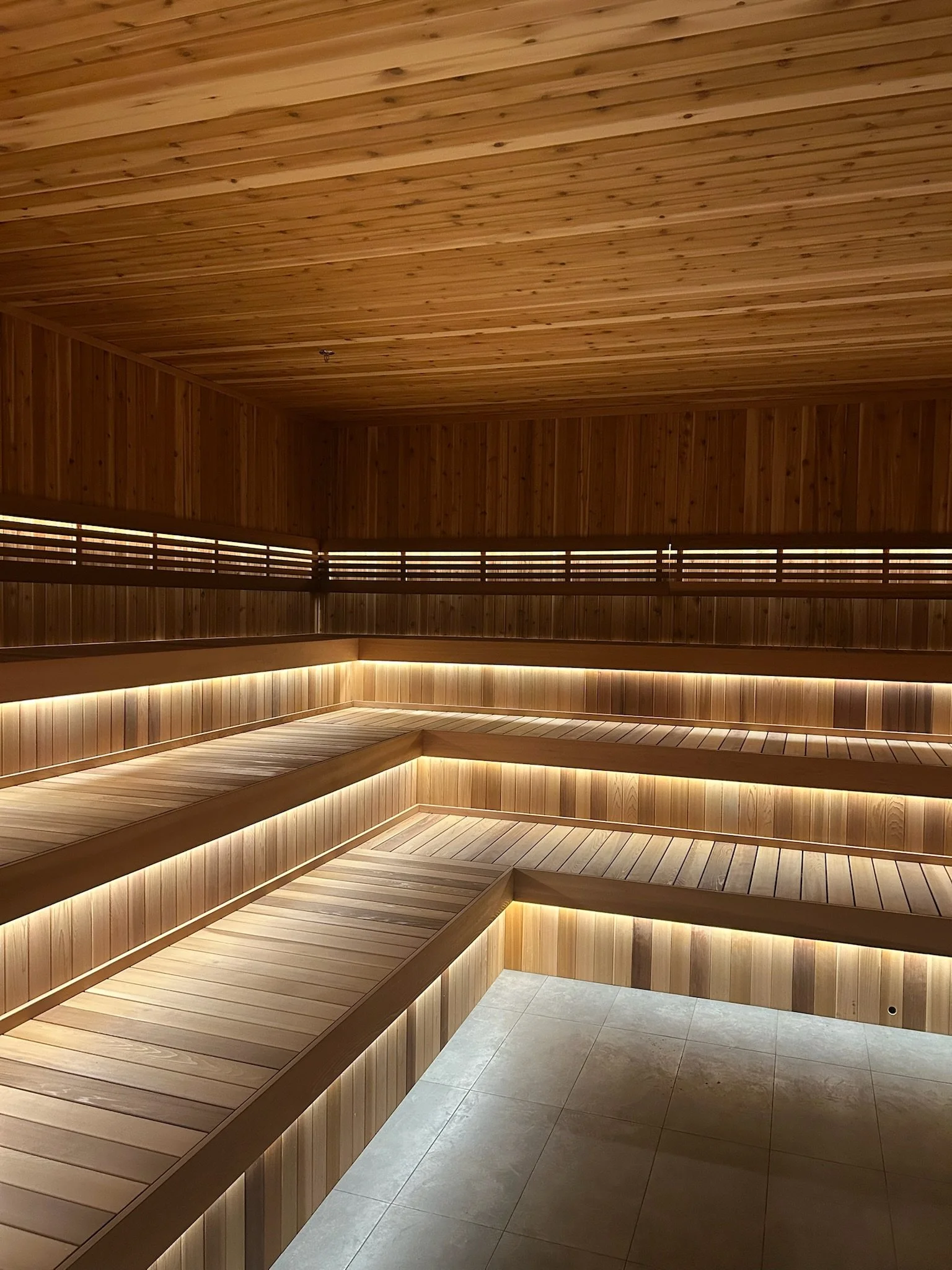 Offline Wellness Club  Indoor sauna with wooden benches and walls, illuminated by LED lighting, next to tiled floor.