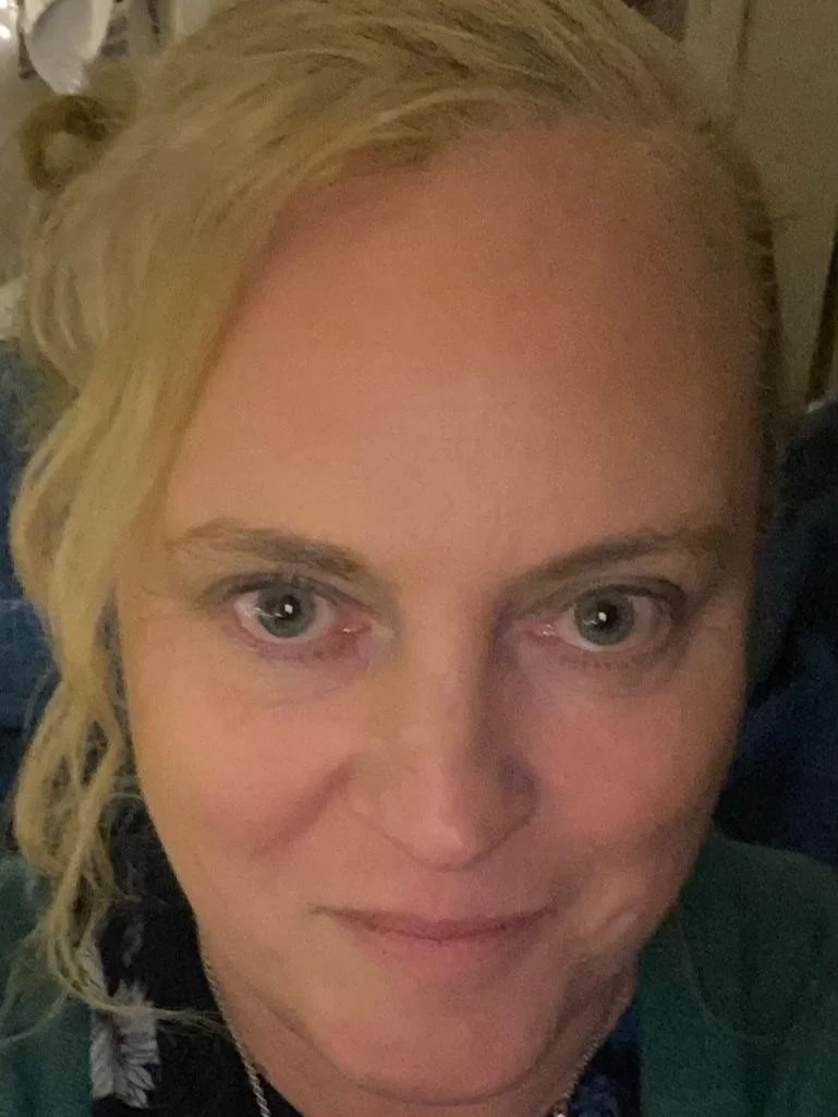 This is Kerry.  Close-up selfie of a woman with blonde curly hair and light-colored eyes, smiling slightly.