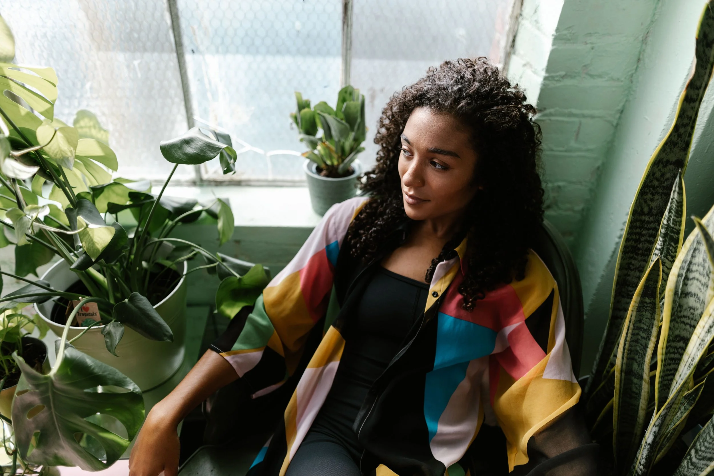 Woman sitting by a window surrounded by plants, online EMDR therapy for Culver City women.