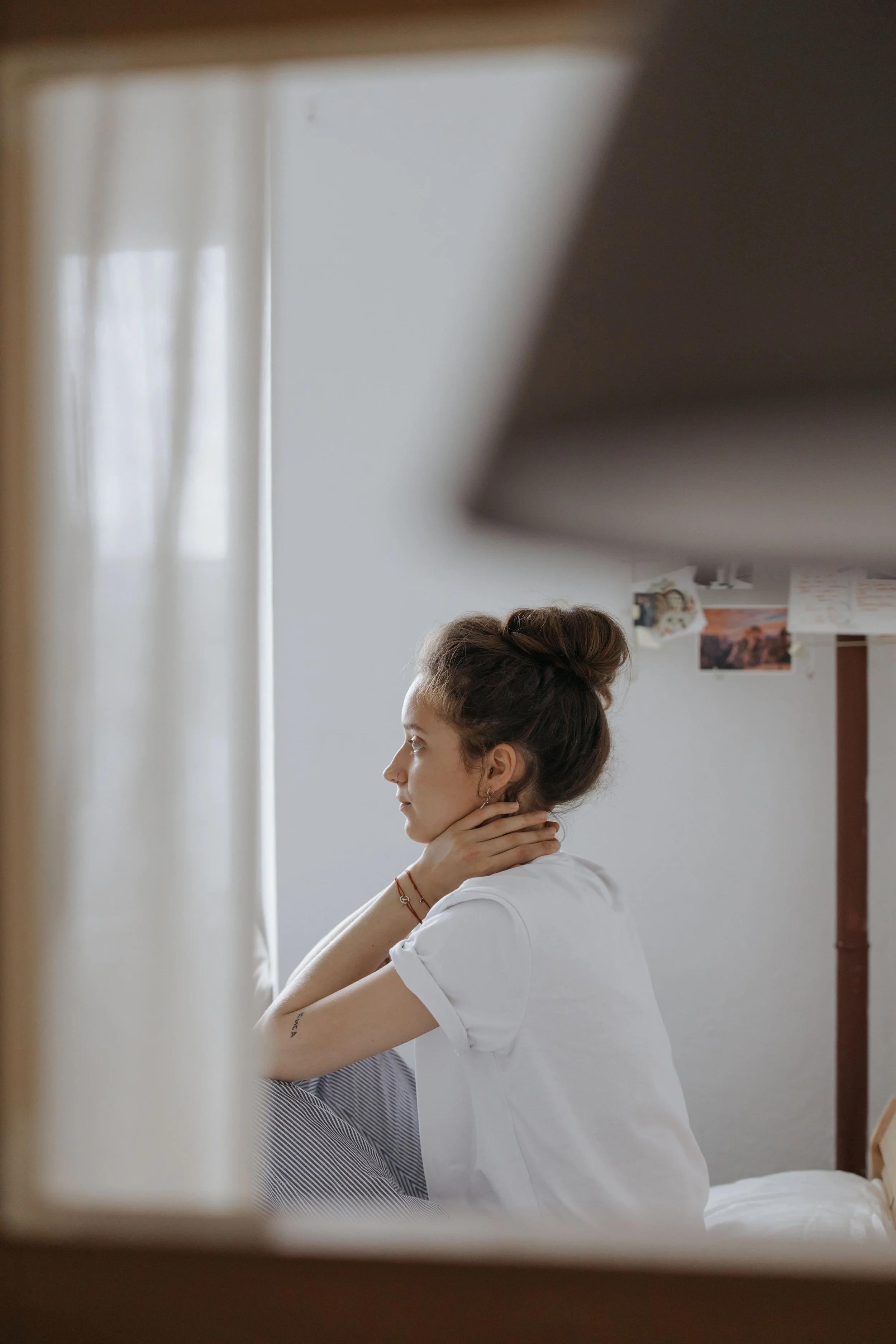 Woman sitting quietly in her bedroom in soft morning light, private and contemplative.