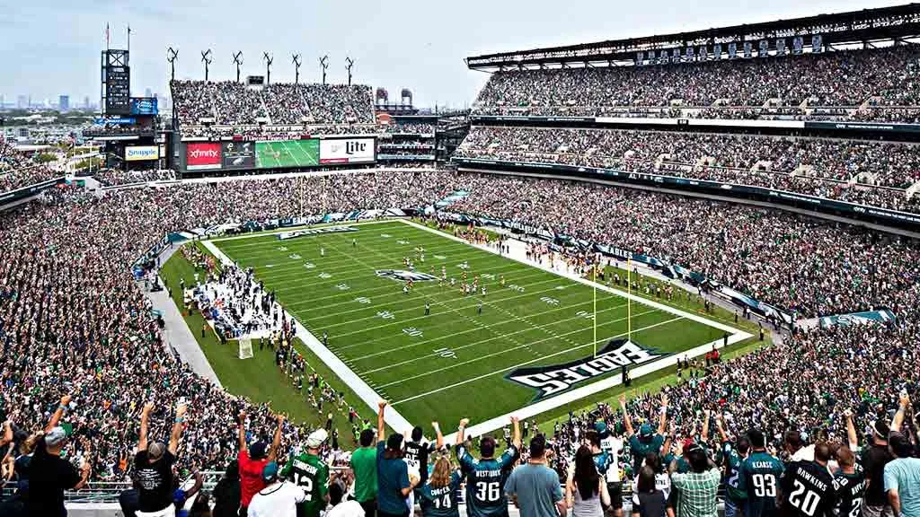 Panoramic view of a packed football stadium during a game, with fans cheering and players on the field.