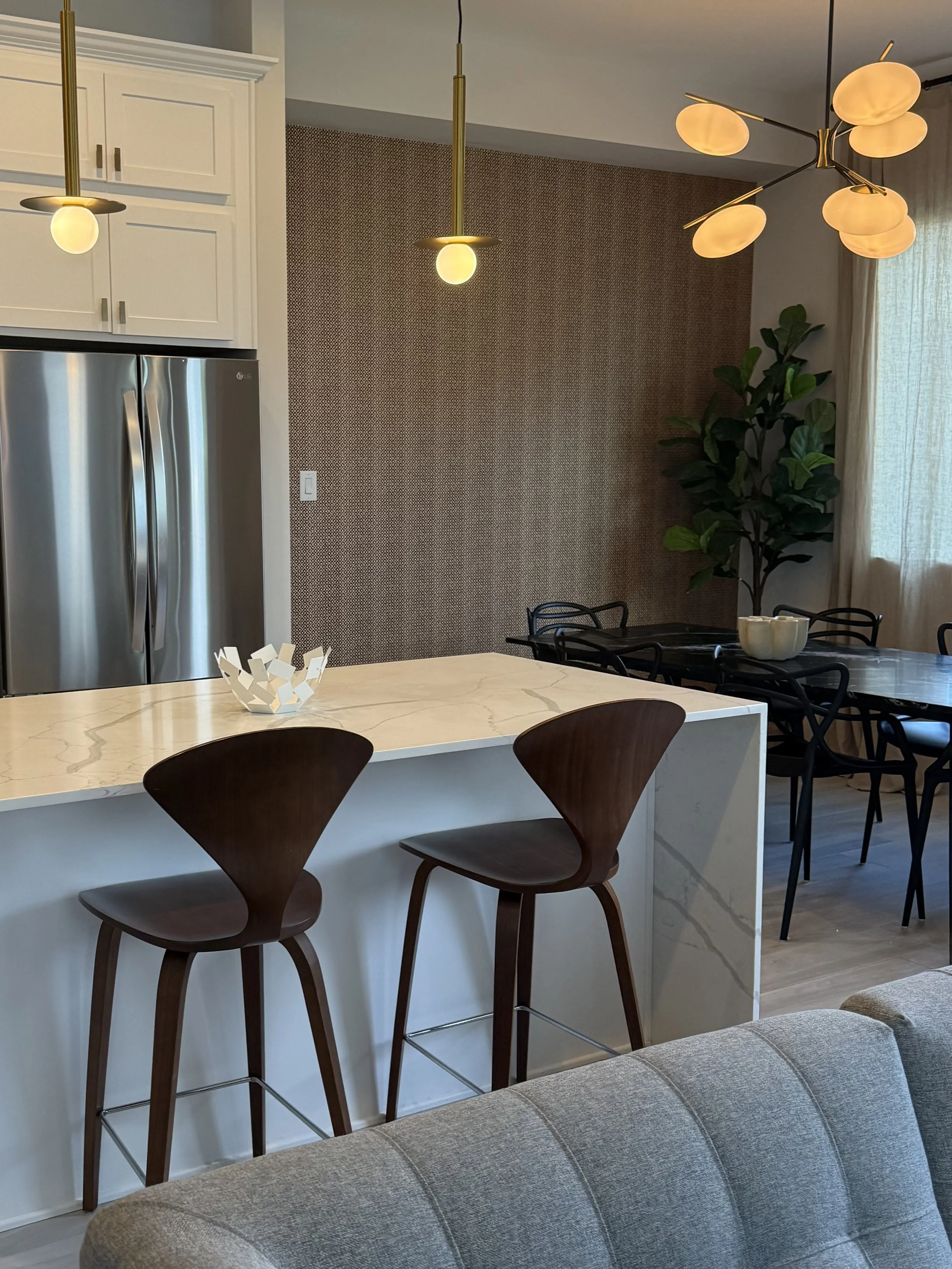 Mid century design with browns and golds, Cristal pendant lighting with a warm light, and black marble table with Philippe Starck chairs produce by Kartell