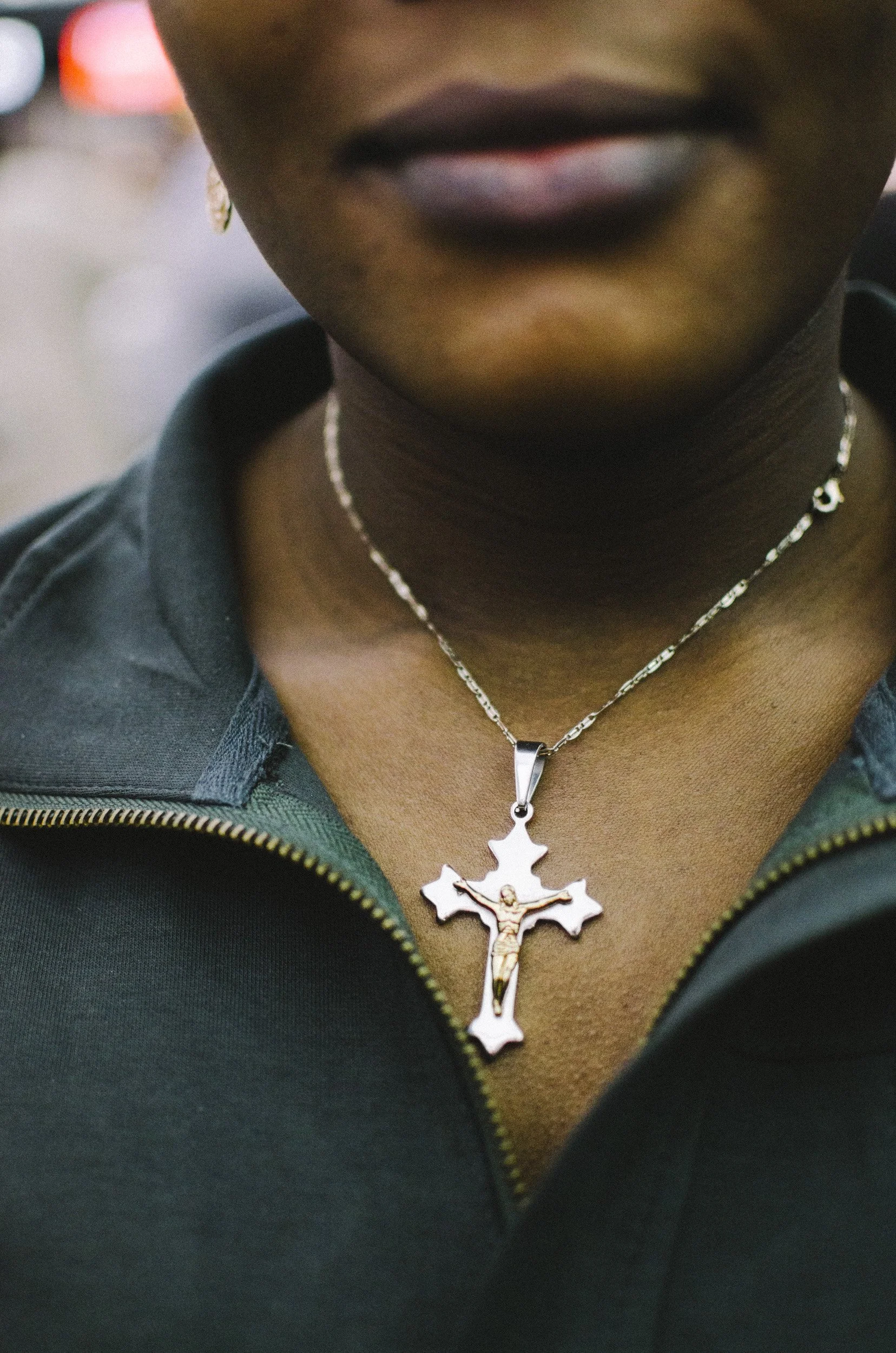 Close-up of a woman wearing a crucifix necklace with a green zip-up jacket and dark lipstick.