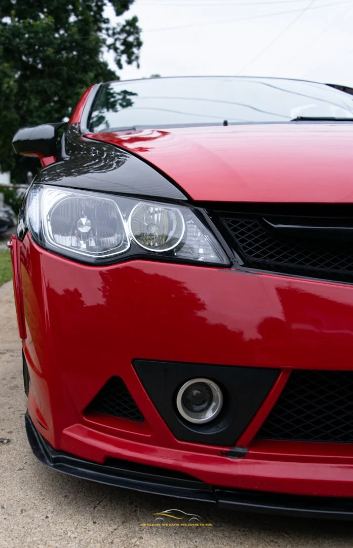 Close-up of the front of a red and black modern sports car showing headlights, grille, and fog light.