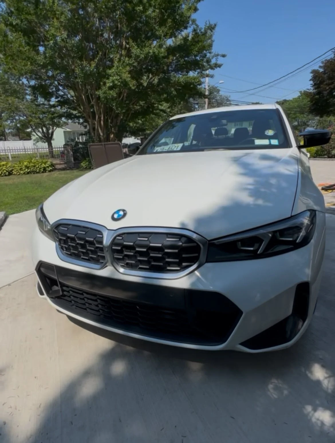 White BMW car parked outdoors on a concrete driveway, with trees and a house in the background on a sunny day.