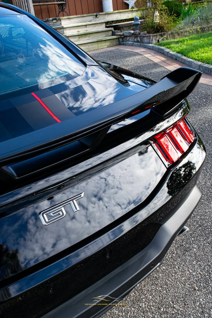 Close-up of the rear of a black sports car with a GT badge, showcasing the glossy paint reflecting the sky and clouds after a ceramic coating performed by Glossfix.