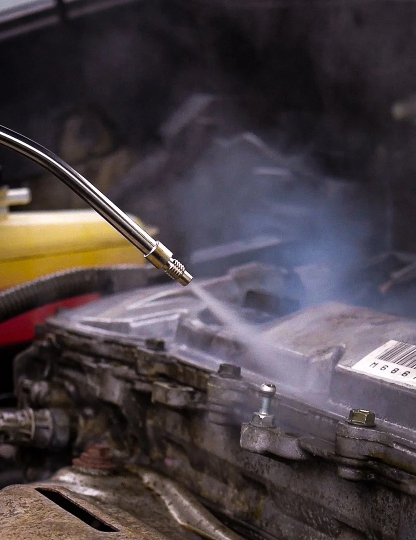 A close-up of an engine being cleaned or serviced with a device emitting steam or spray onto the engine components.