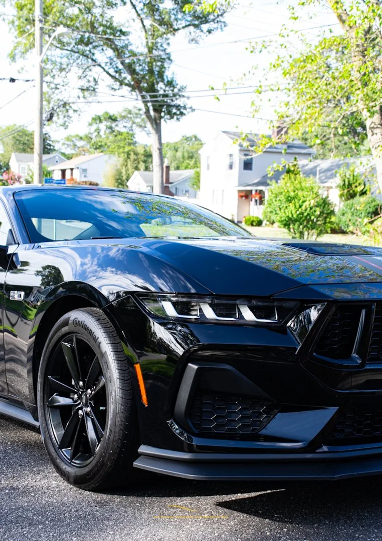 A black sports car parked on a suburban street with houses and trees in the background.