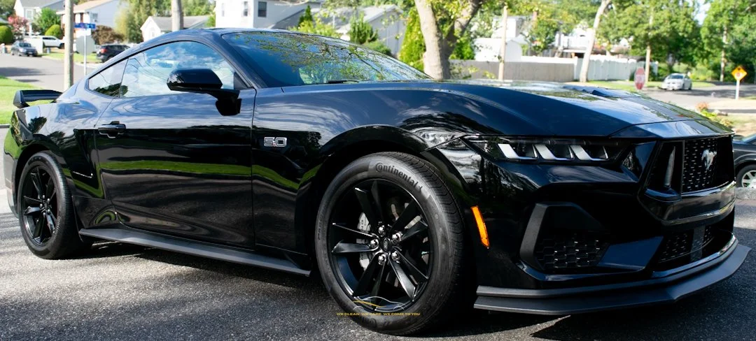 Black sports coupe car parked on a residential street with trees and houses in the background.