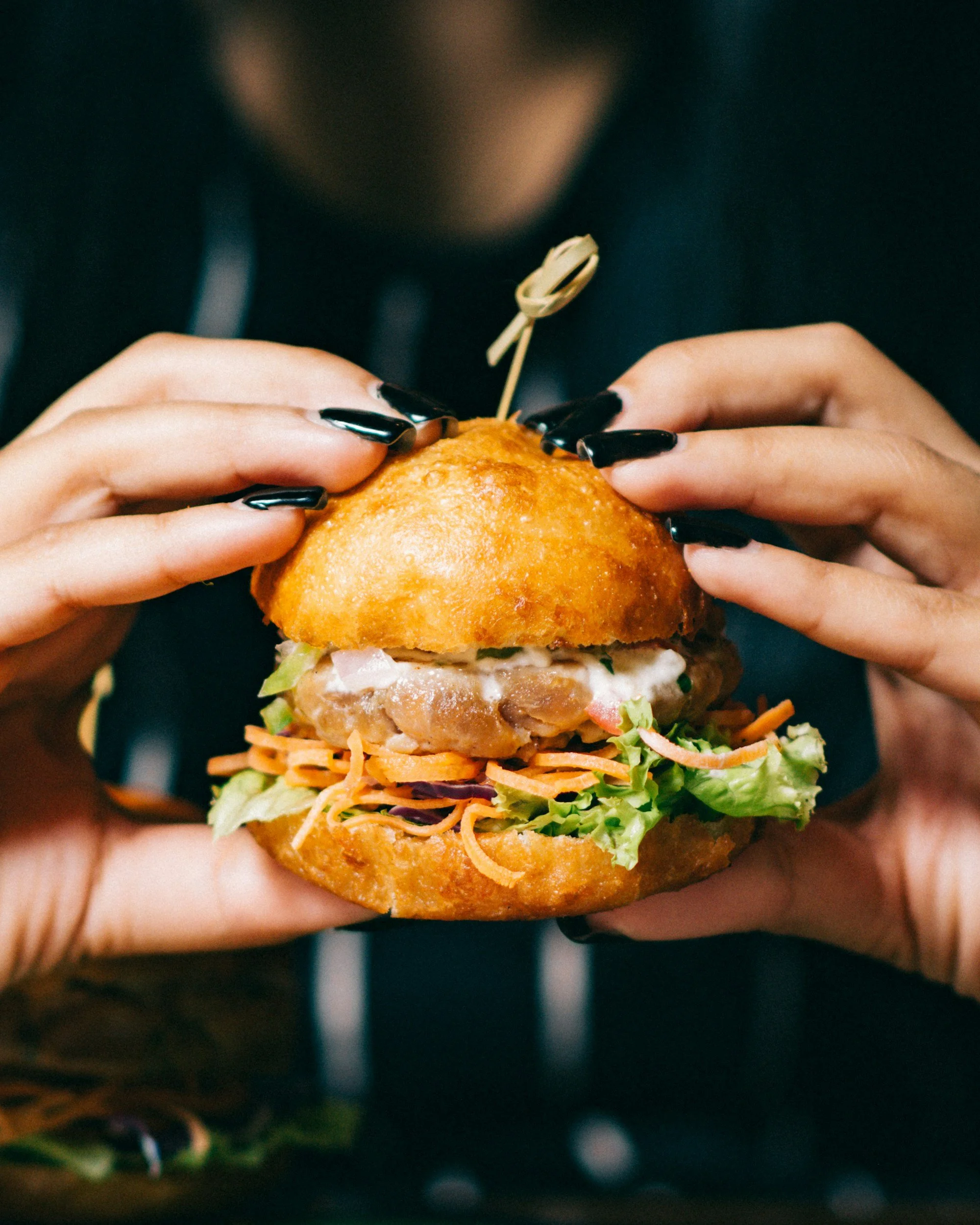 Photo of a person with black nail polish holding a burger.