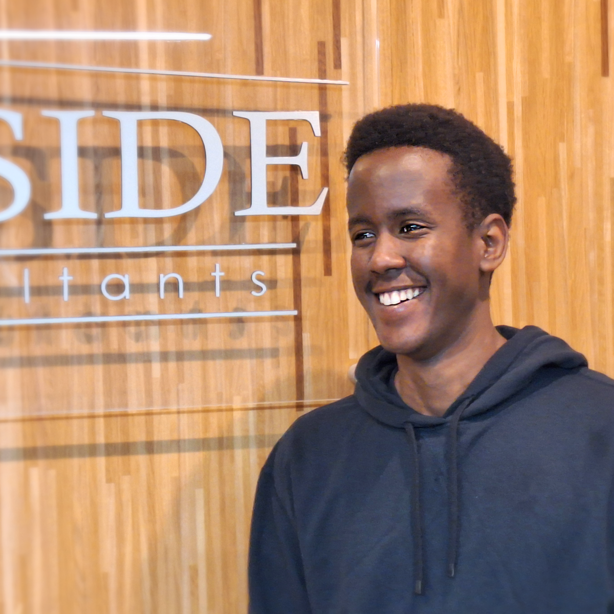 Bryan Rusagara posing in front of the Harbourside Engineering Consultants sign in the Dartmouth Office, 2025