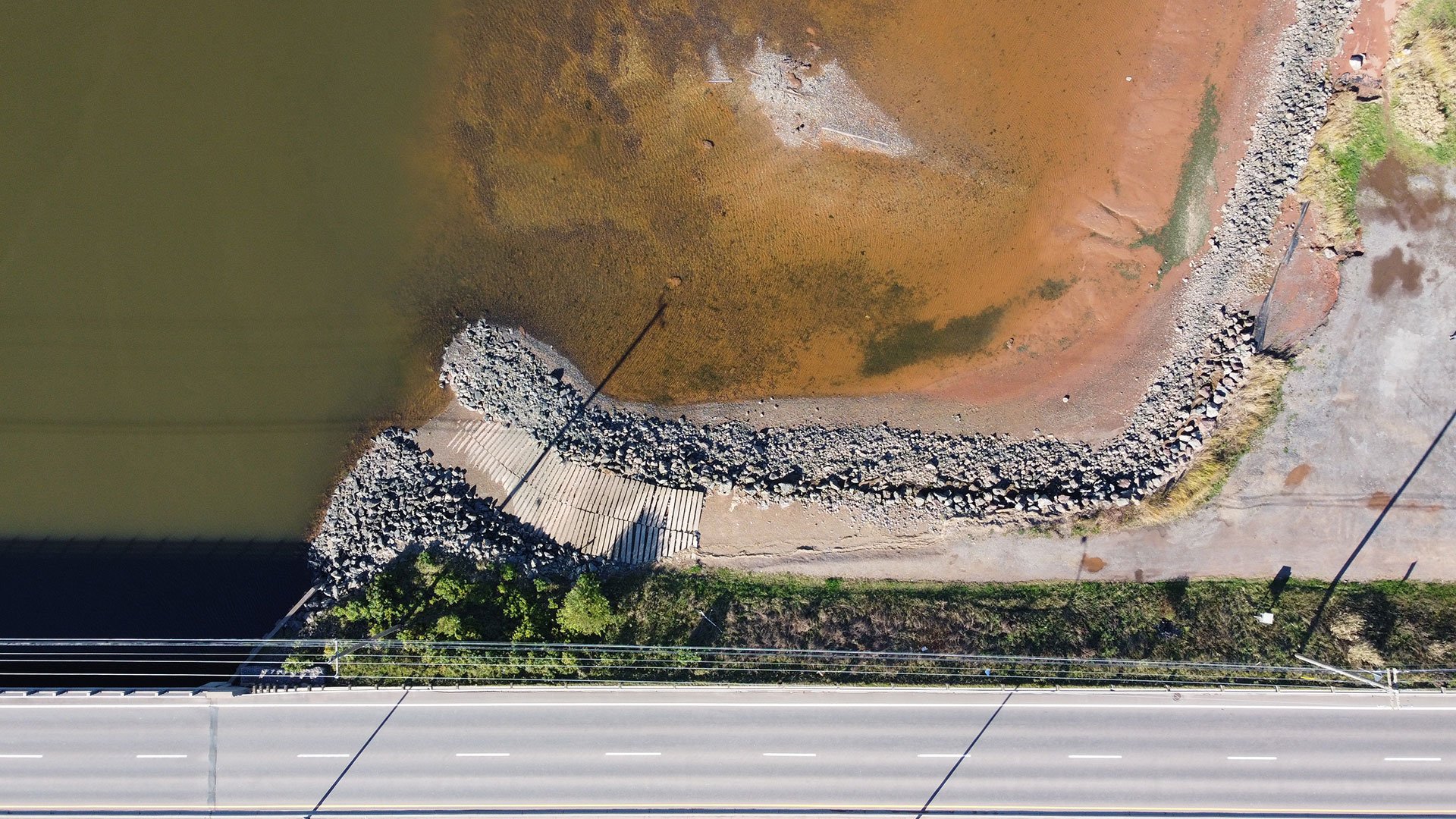The original North River Slipway, after sustaining damage from Hurricane Fiona. This image was taken during a drone survey prior to redesign. The slipway can be seen adjacent to a roadway, as seen from directly above. Water surrounds the structure.