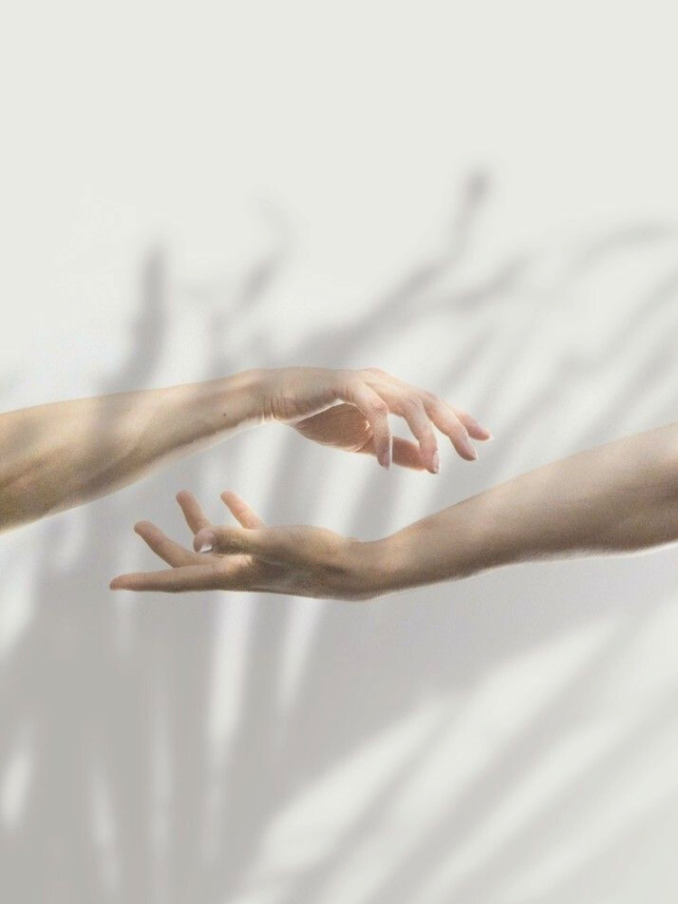 Two hands reaching towards each other, with soft shadows cast on the background.