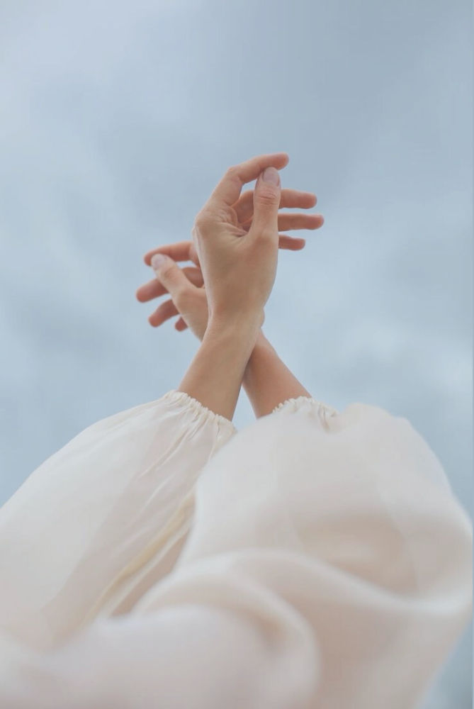 Close-up of a person reaching upward with hands against a cloudy sky.