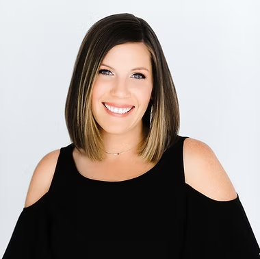 A woman with shoulder-length brown hair smiling, wearing a black top with shoulder cut-outs against a light background.