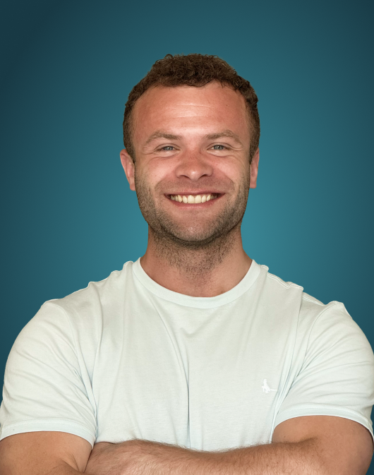 Smiling man with short curly hair wearing a white t-shirt, crossing arms, against a blue background.