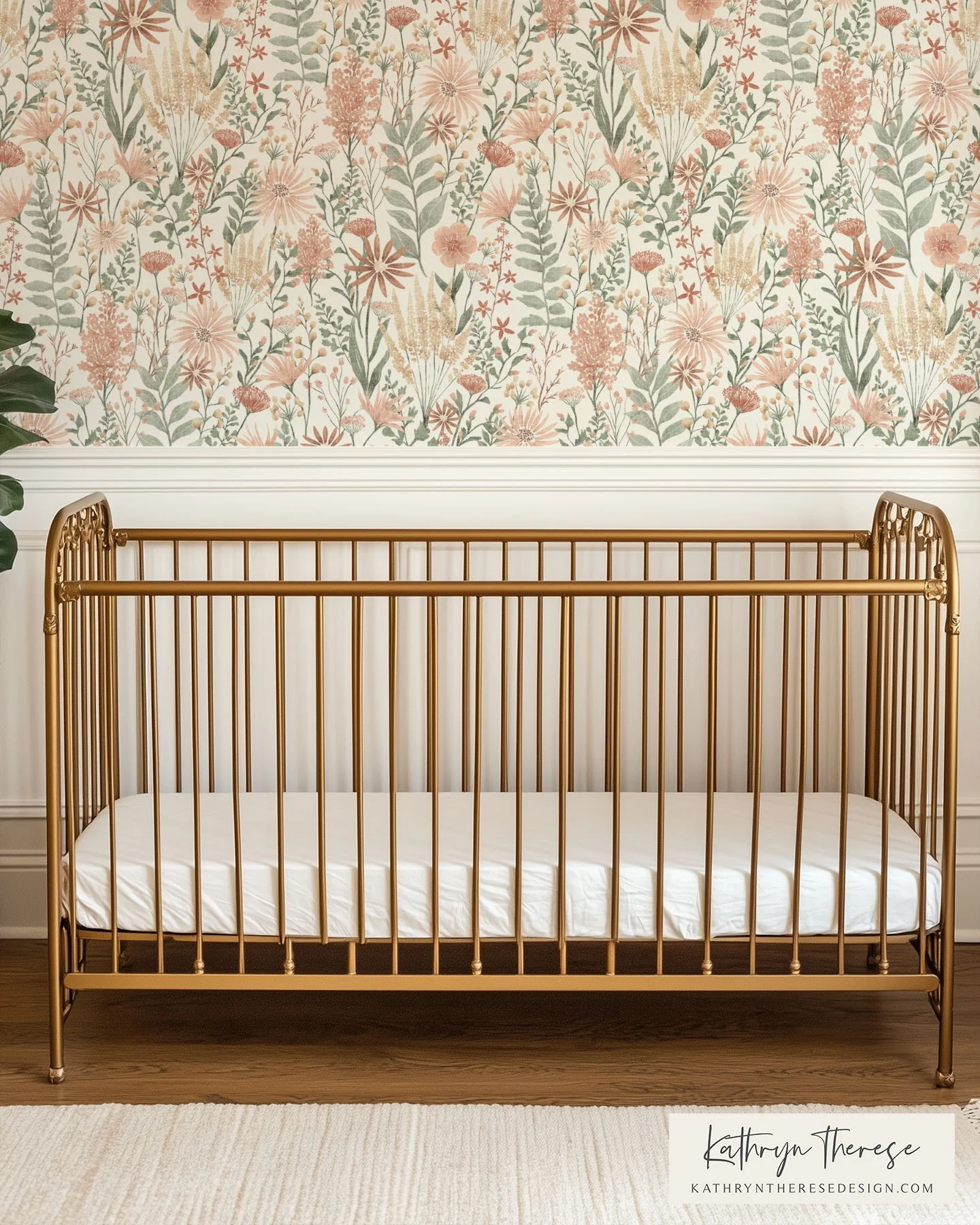 A gold metal crib with a white mattress in a room with floral wallpaper and cream a beige rug.