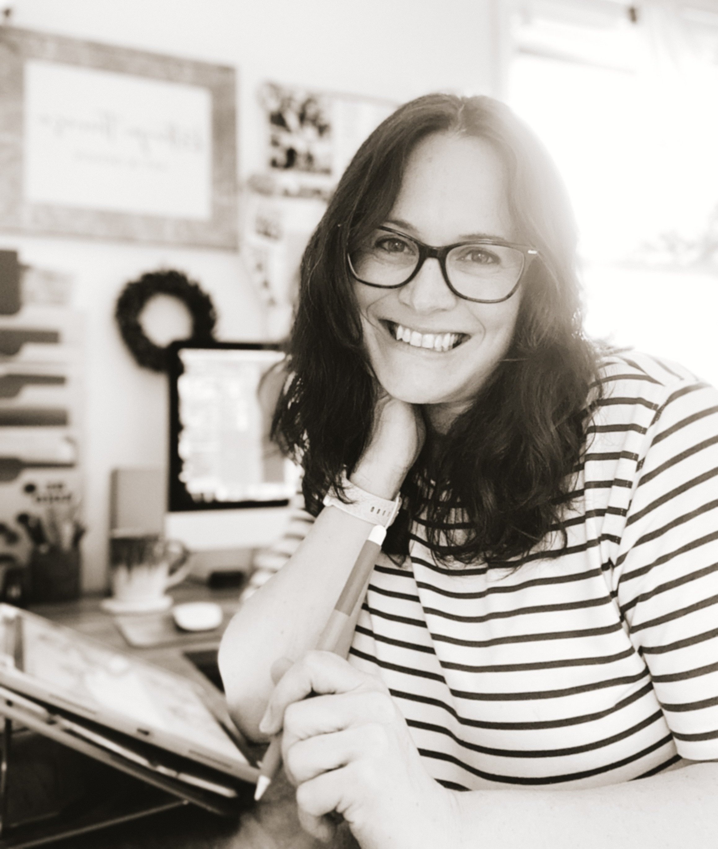 Kathryn Therese, a surface pattern designer, sitting at her desk with a computer and art supplies, in creative home office space.