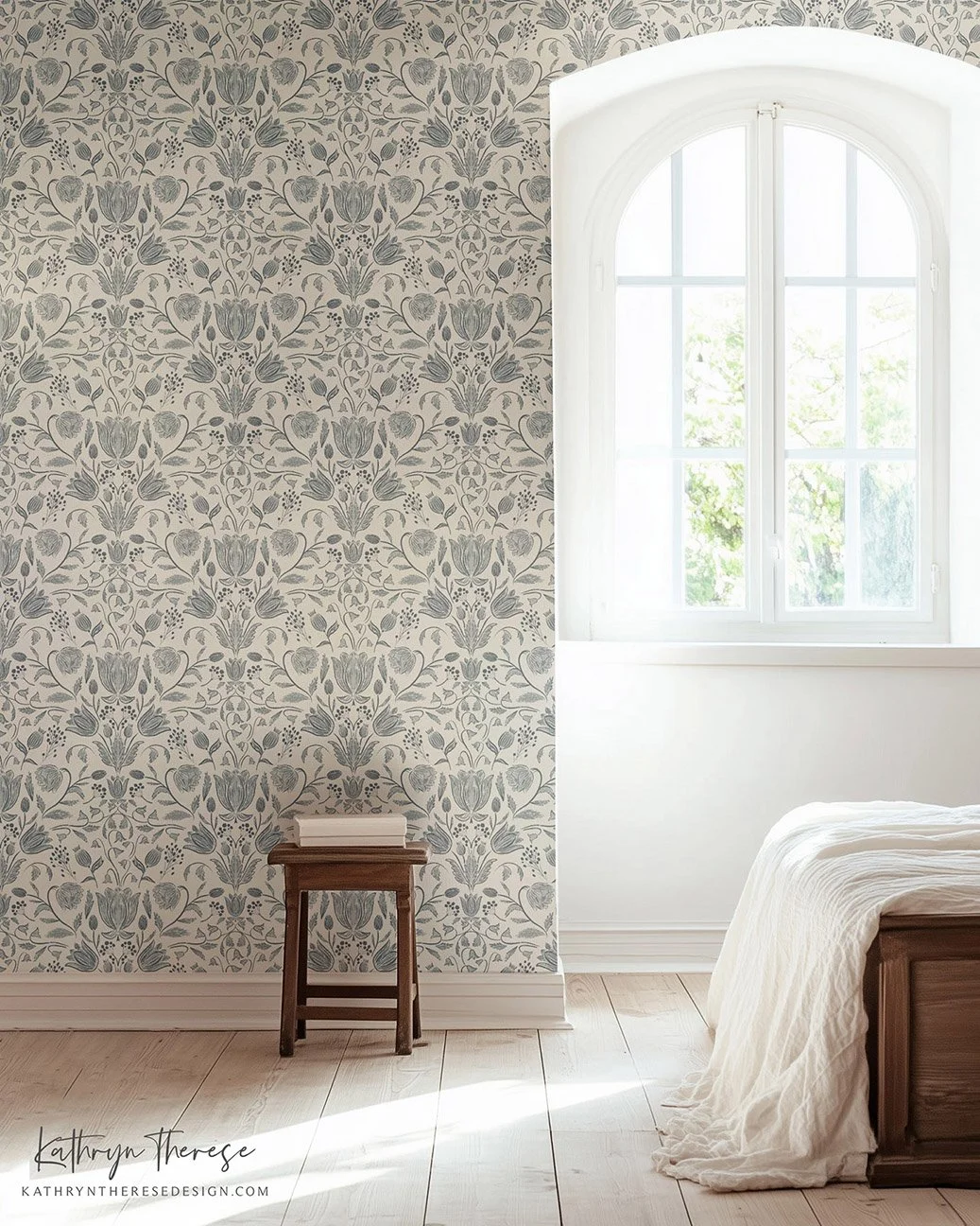 A corner of a bedroom with a window, patterned wallpaper, a small wooden stool with a white cloth on top, and a bed with a white blanket.