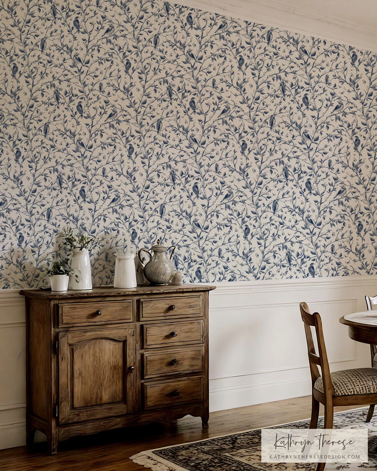 A vintage wooden sideboard with three drawers and one cabinet, decorated with white and gray vases and a plant, against a wallpaper featuring blue birds and branches in a room with wooden flooring and a chair with a patterned cushion.