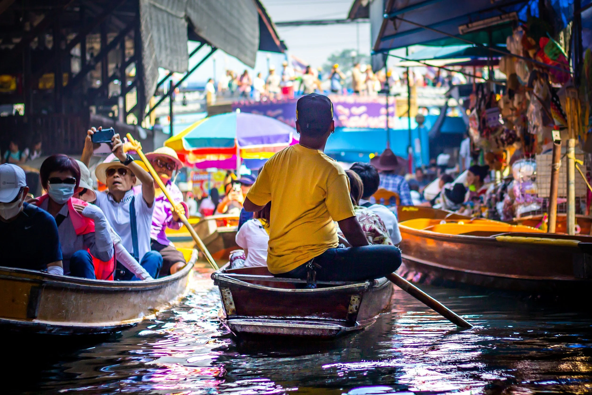 Marché flottant avec des bateaux et des touristes, stand de vendeurs d'objets artisanaux, parasols colorés, activité animée sur l'eau en journée