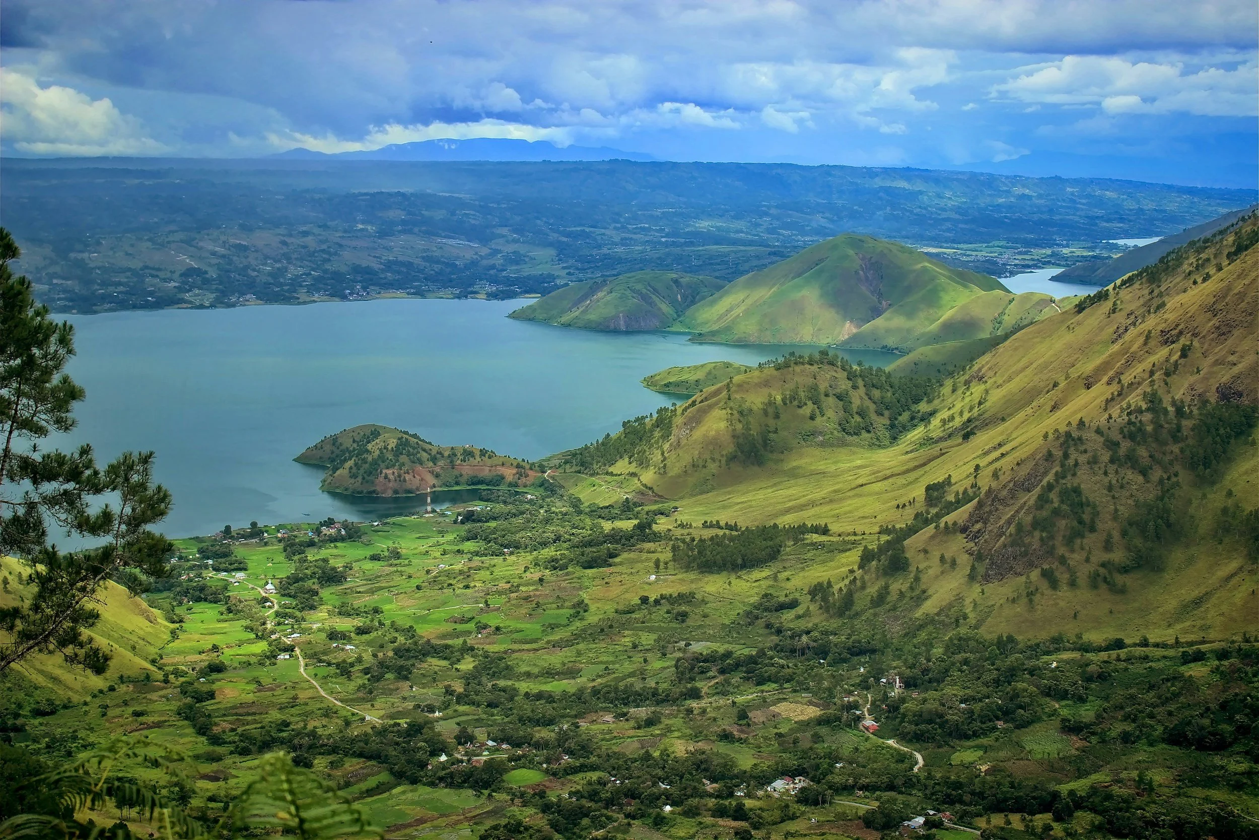 Paysage de montagnes verdoyantes autour d’un lac, avec un ciel nuageux
