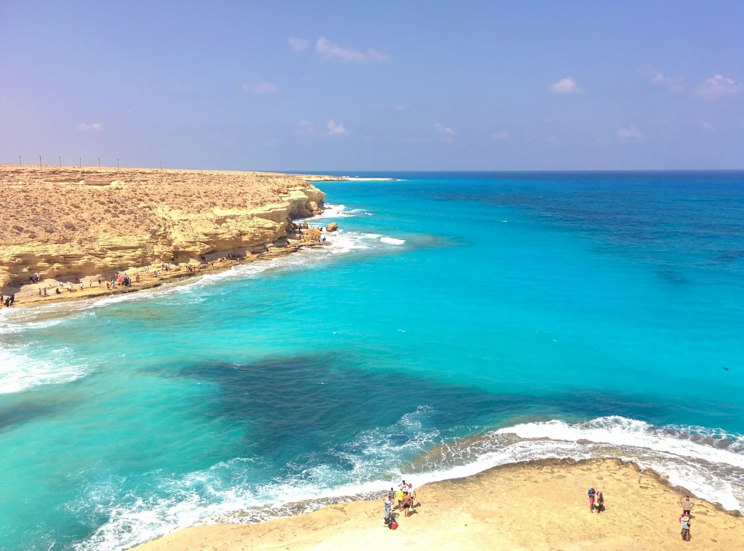 Côte rocheuse avec eau turquoise et plages, plusieurs personnes se trouvent sur la plage et sur les rochers.
