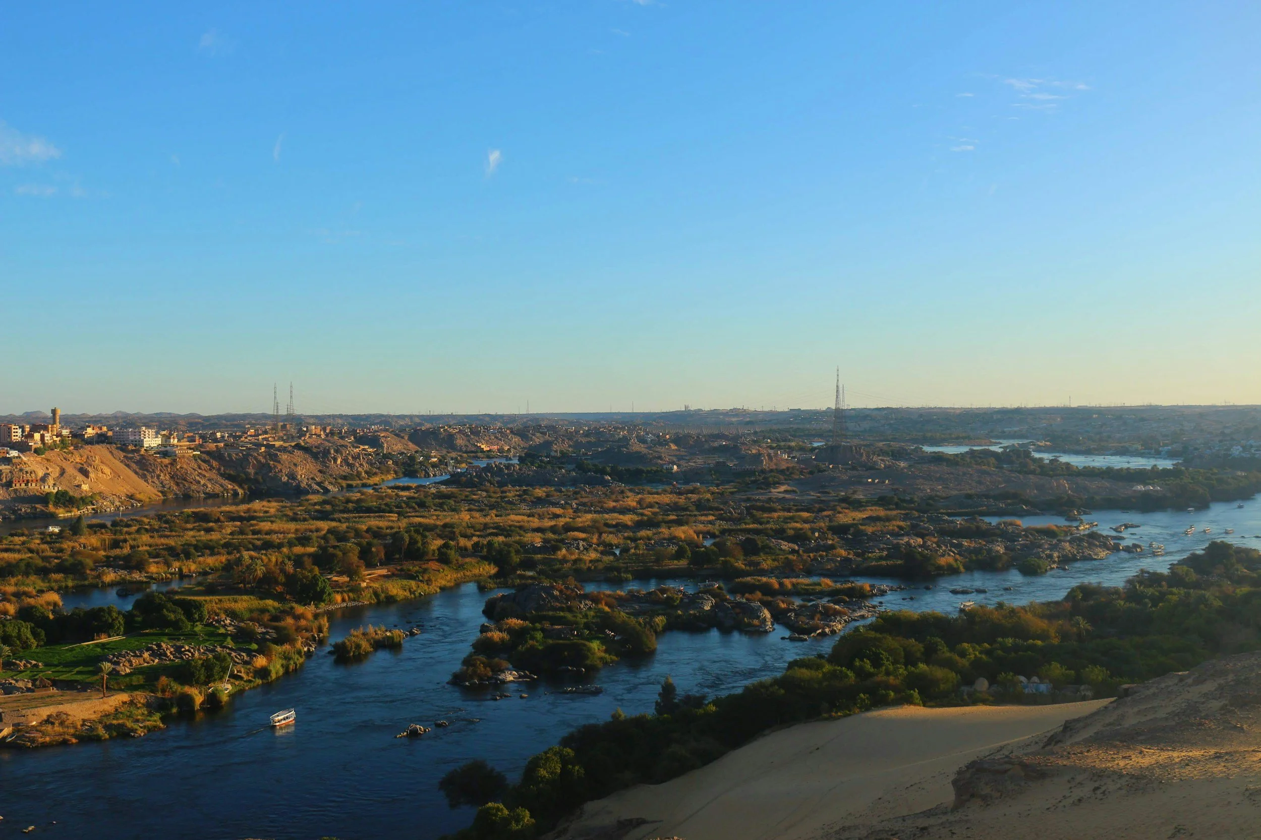 Paysage de la ville avec rivière serpentant à travers des zones verdoyantes et des collines, au coucher du soleil, avec un ciel bleu clair et quelques nuages