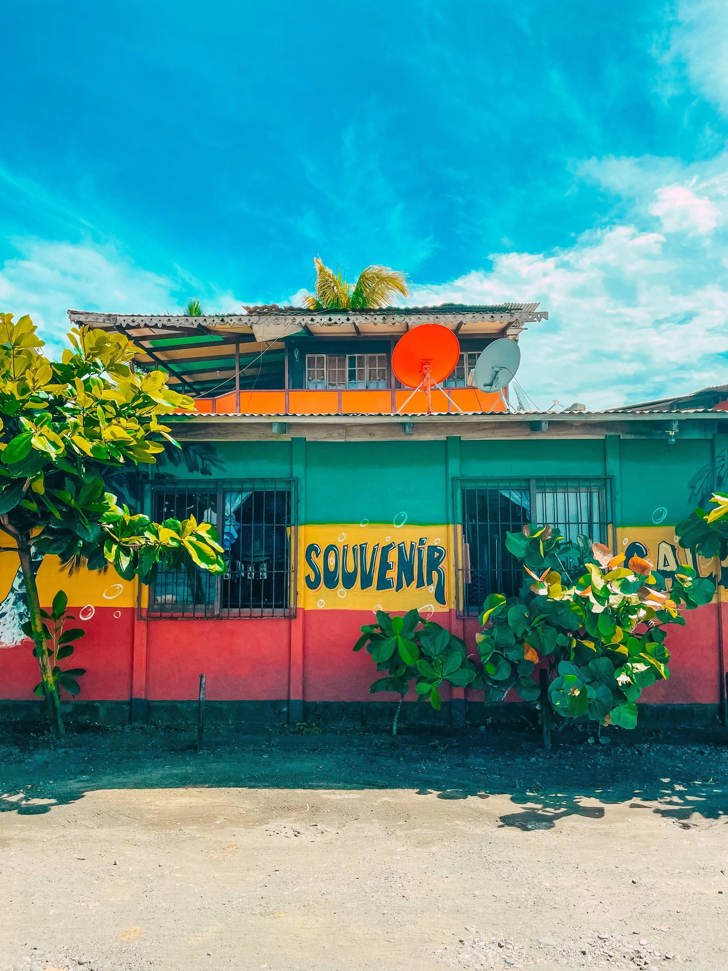Une maison colorée avec le mot « Souvenir » peint sur la façade, entourée d'arbres verts et sous un ciel bleu clair.
