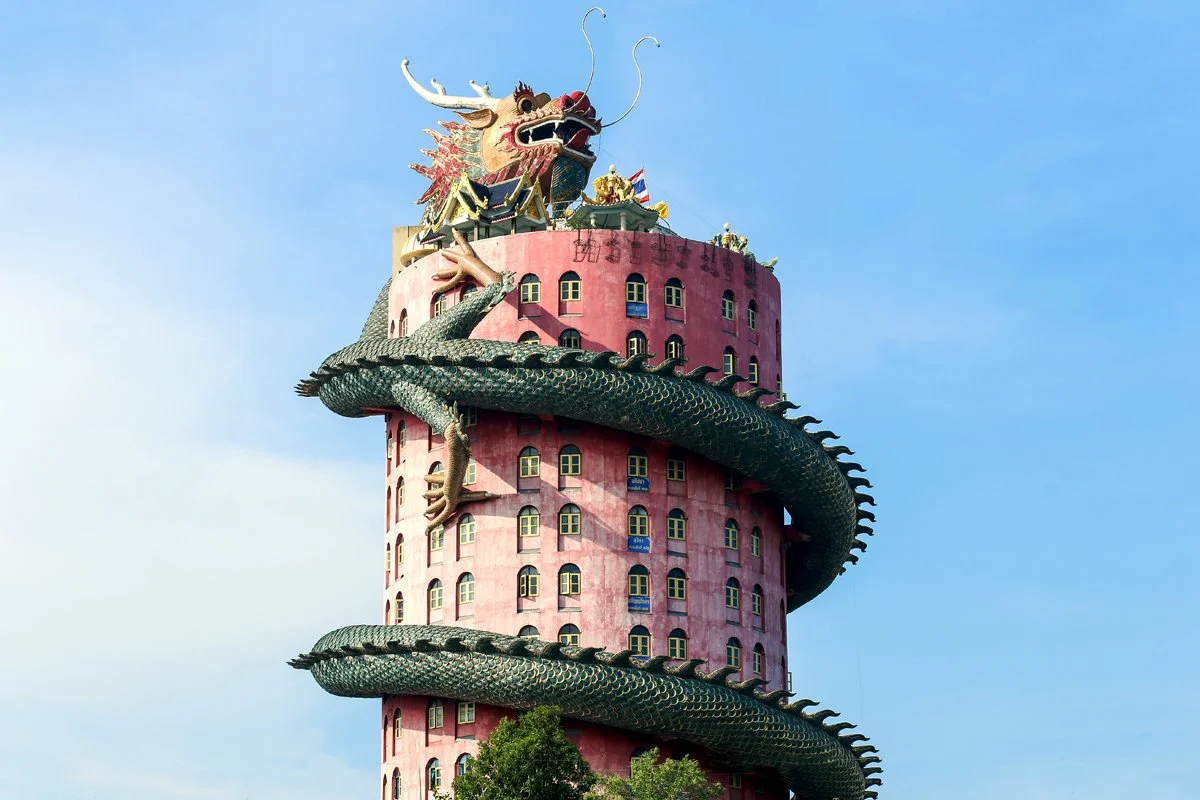 Une tour rose avec un dragon et un serpent enroulés autour, en haut de la tour, avec un ciel bleu en arrière-plan.