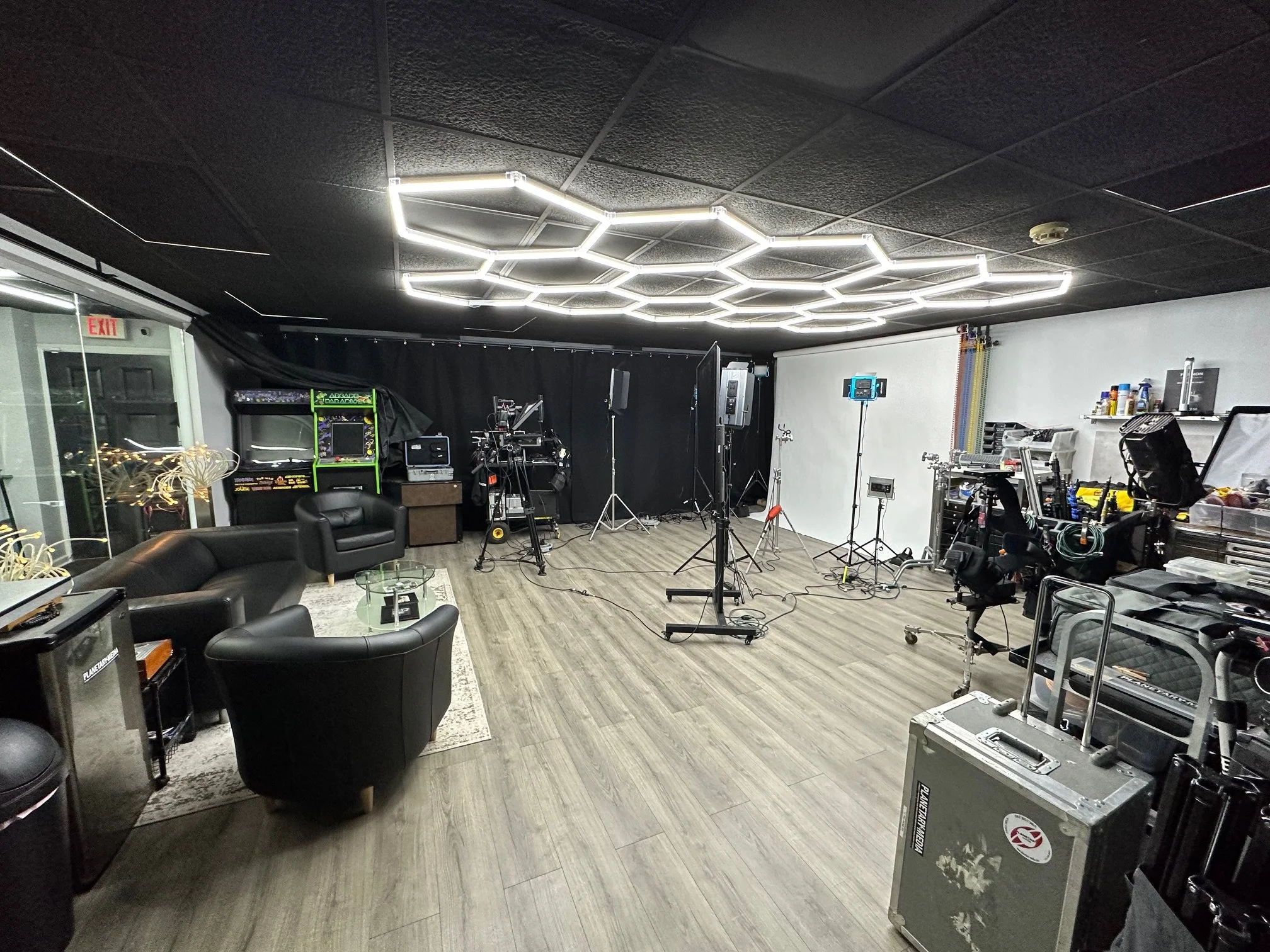 A professional photography and video studio with lighting equipment, cameras, and seating, featuring modern geometric ceiling lights.