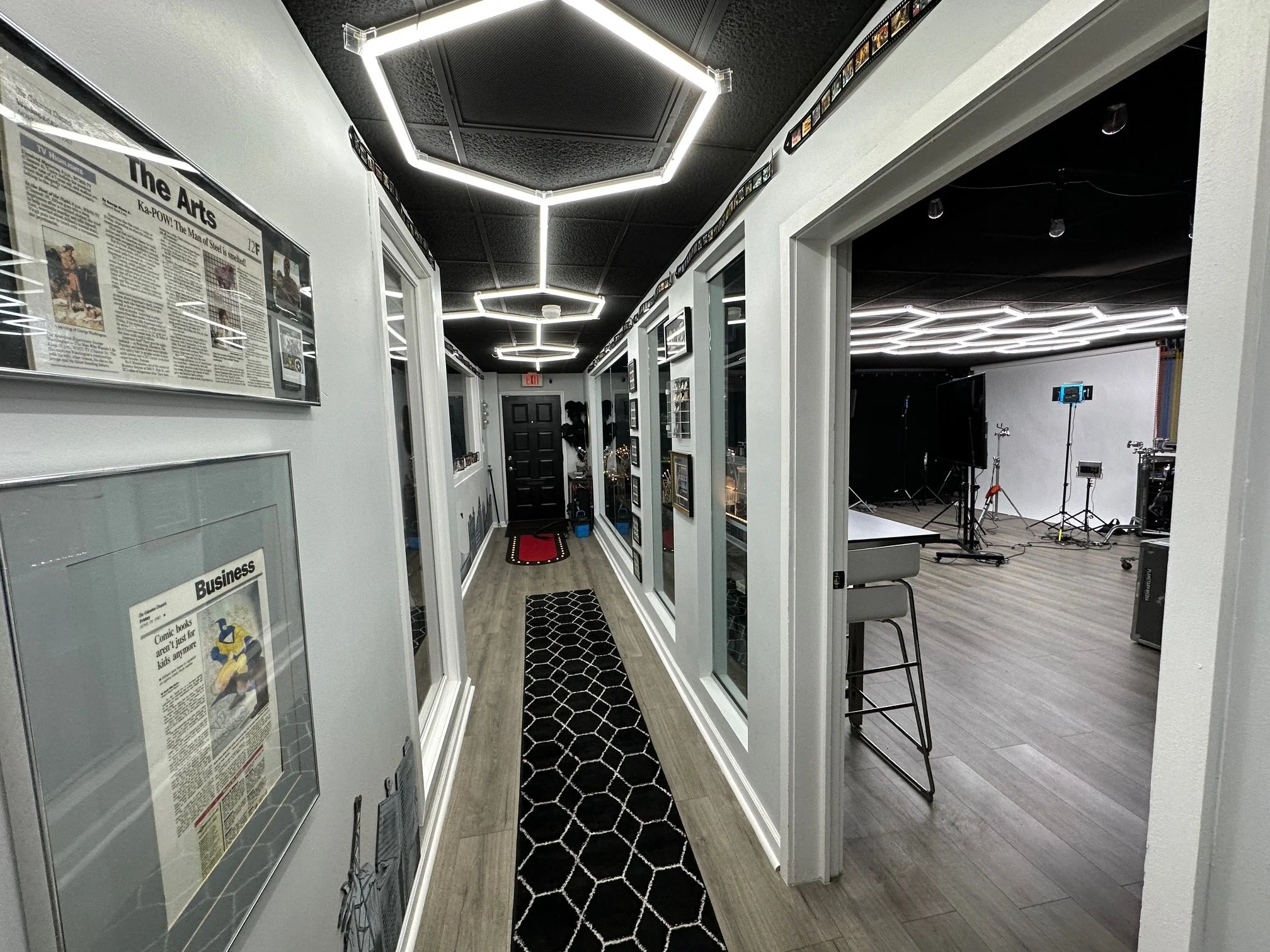 A hallway leading to a studio with lighting, cameras, and microphones, with framed newspapers on the wall along the corridor.
