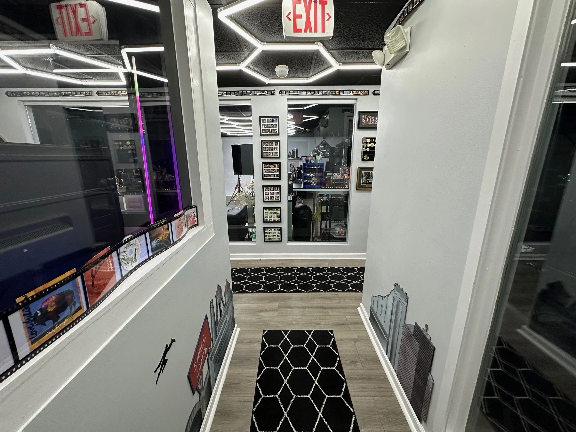 Interior view of a modern room with framed pictures on the walls, a black and white rug, a glass partition, and neon ceiling lights.