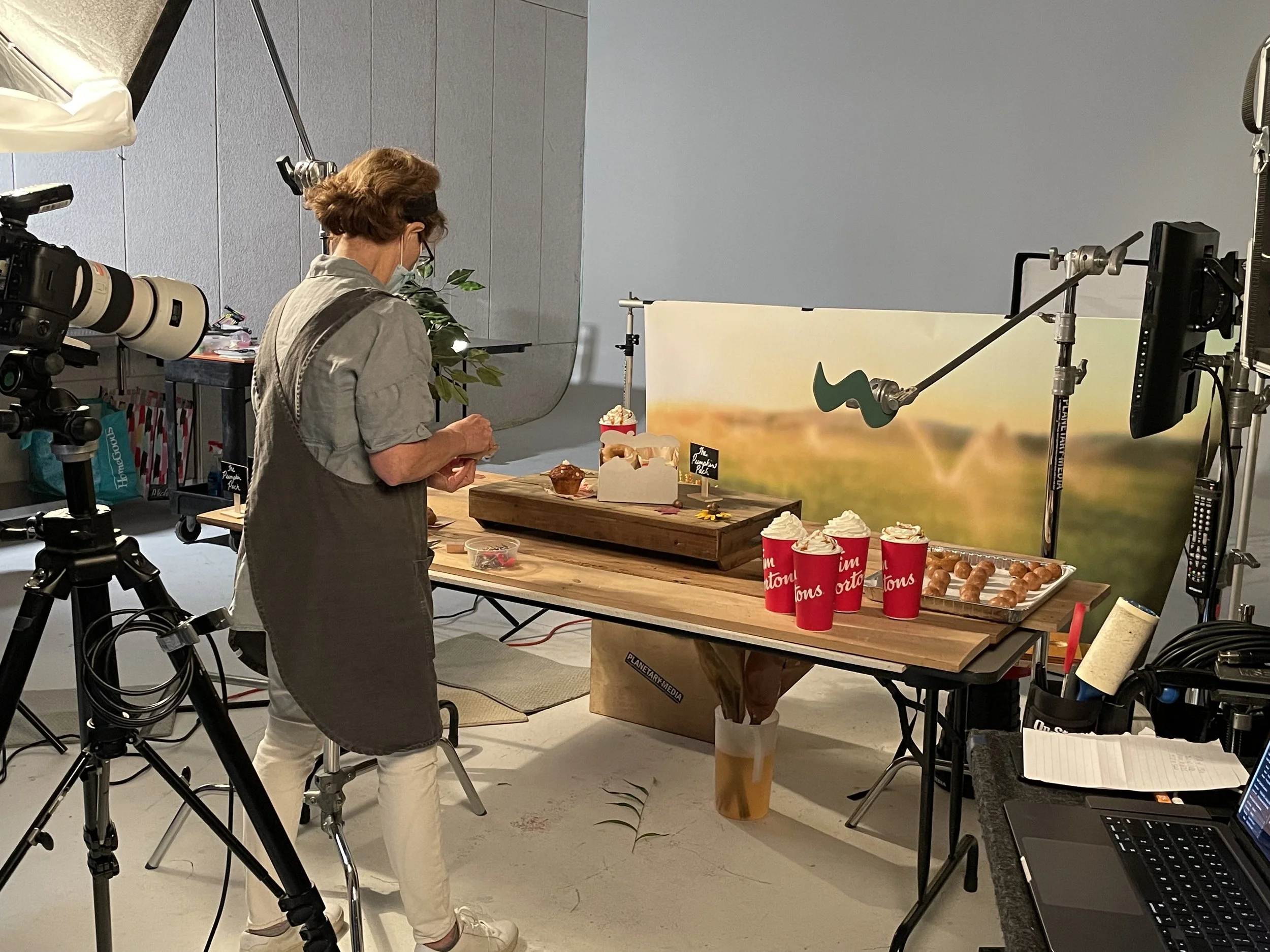 A woman setting up a food display on a table in a studio, with professional filming equipment and lighting around her.