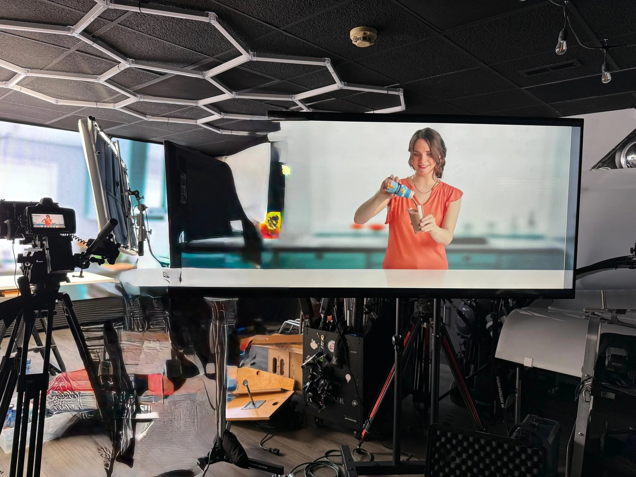 Studio setup with a large screen showing a woman pouring a drink, possibly in a promotional or commercial video shoot.