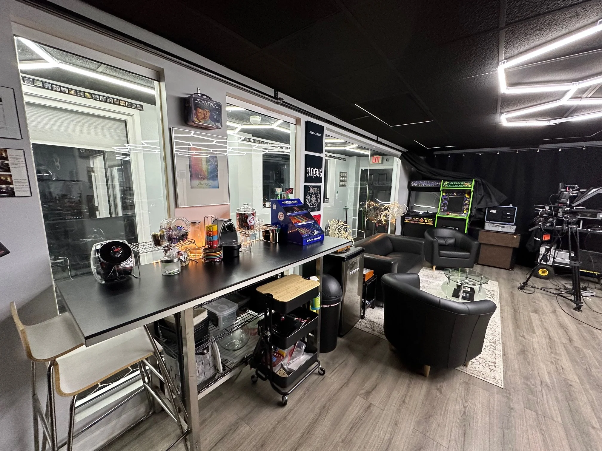 Indoor entertainment lounge with black leather chairs, arcade games, and music equipment, illuminated by modern LED lighting.