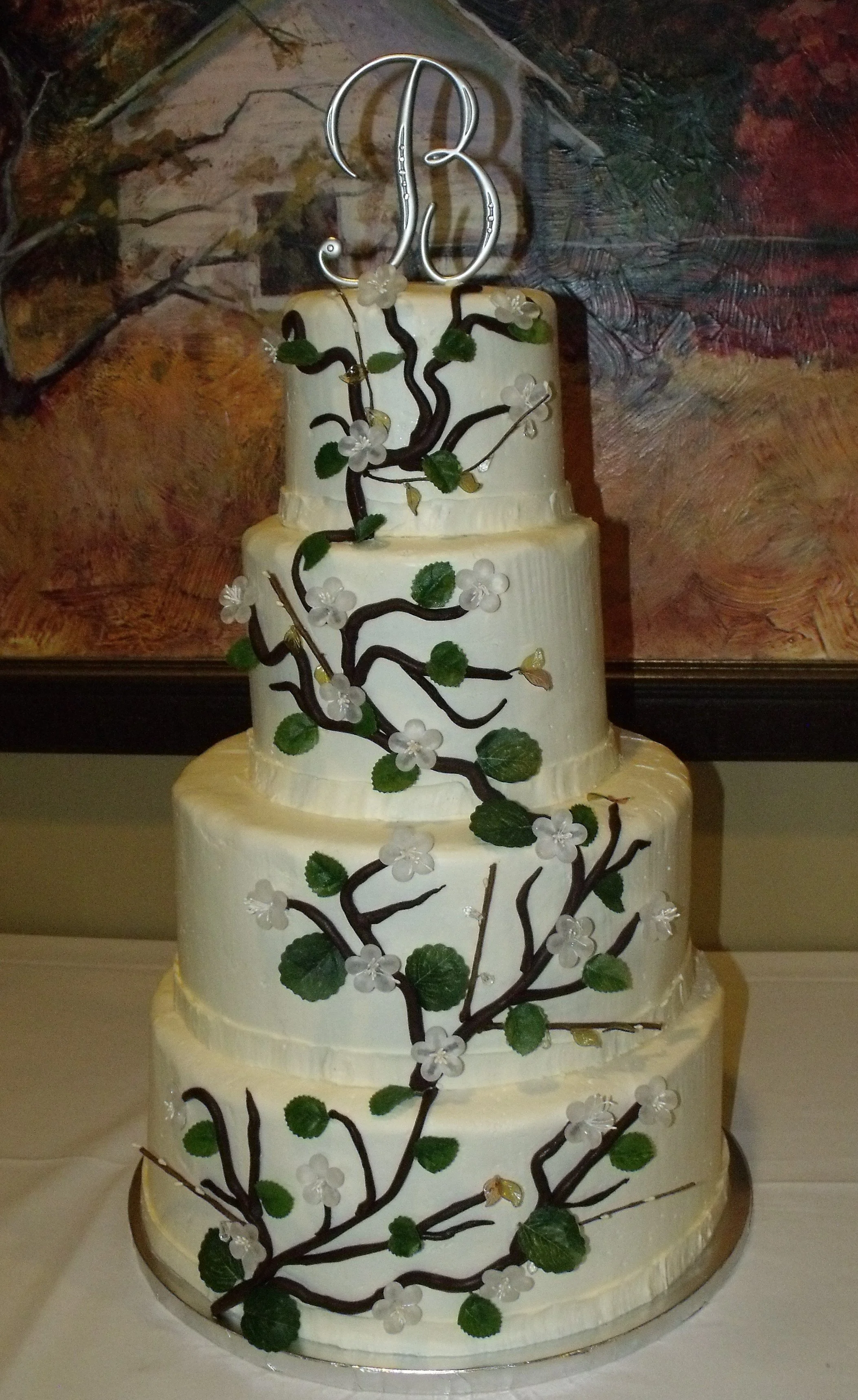 Wedding Cake Four Tier Smooth Side Buttercream Tower Aligned to the Back Hand Applied Rolled Chocolate Branches with Crystal Cherry Blossoms and Leaves Silver Monogram Cake Topper