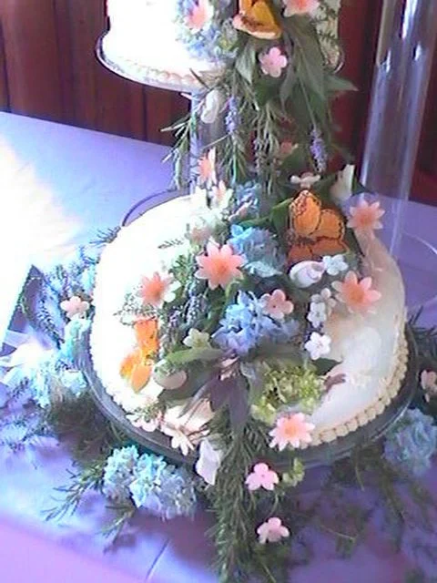 Wedding Cake with Sugar Porcelain Butterflies and Wild flowers Cascade over Fresh Greens