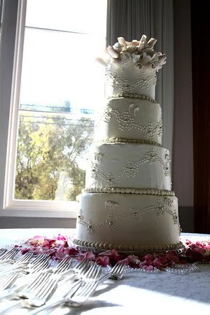 Four tier stacked rounded top edge buttercream frosted classic wedding cake bottom borders piped pearls piped buttercream pearl dot design on cake sides accented with metallic silver pearls cake top arrangement soft pink sugar porcelain rose buds whi