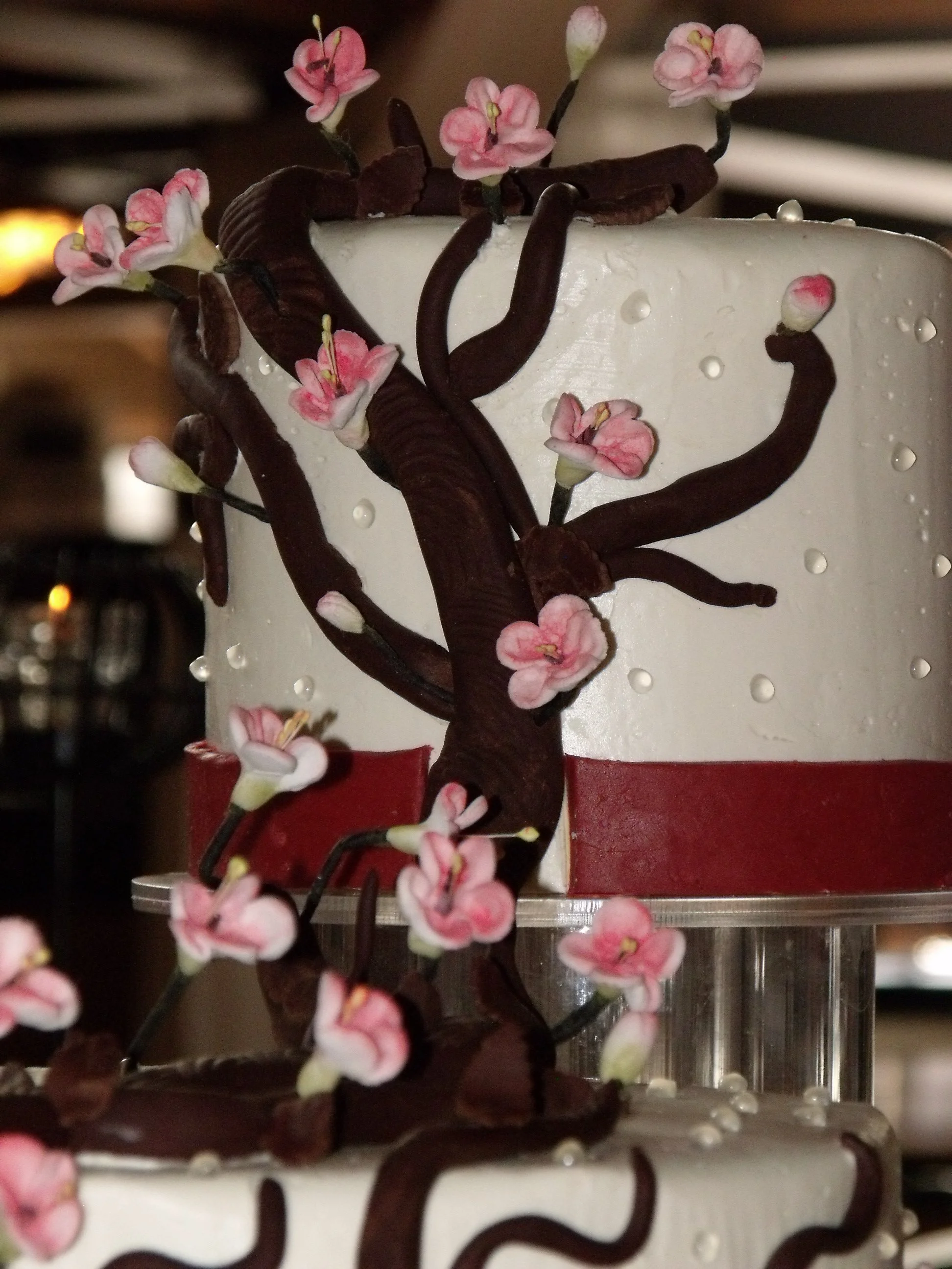 Closeup Sugar Porcelain Cherry Blossoms Hand Rolled Chocolate Tree Branches and Clear Piped Pearls Red Fondant Bottom Ribbon Band 