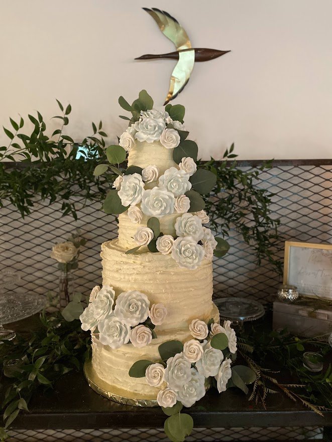 Romantic Rose Wedding Cake Four Tier Stacked Rough Frosted Horizontal Buttercream Sides and Tops of Tiers Over Forty Sugar Porcelain White and Pale Pink Dusted Full Open and Floribunda Roses Simple Fresh Rose Greens Back Flowers