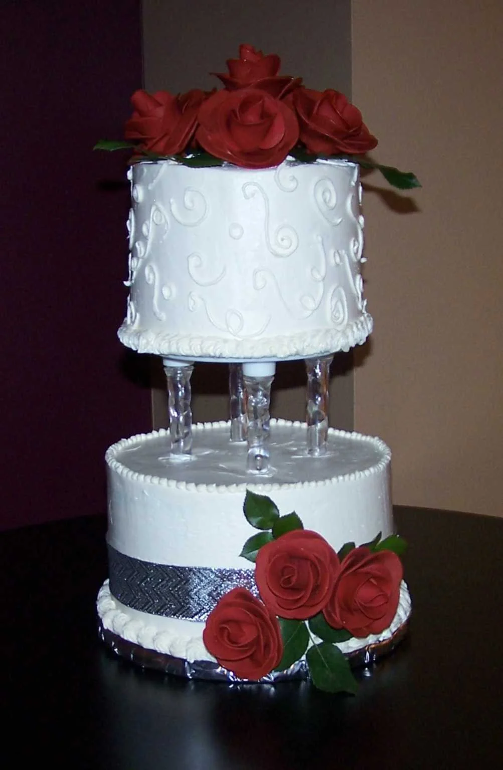 Two Tier Round crystal separated white white wedding cake piped buttercream scroll decor full open red sugar porcelain rose bouquets on side and top fresh rose greens dark metallic silver ribbon surround base cake 